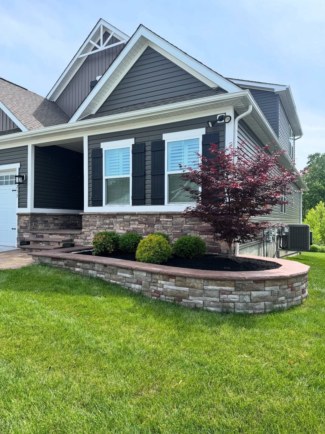 Modern home exterior with stone landscaping, shutters, and colorful shrubs on a sunny day.