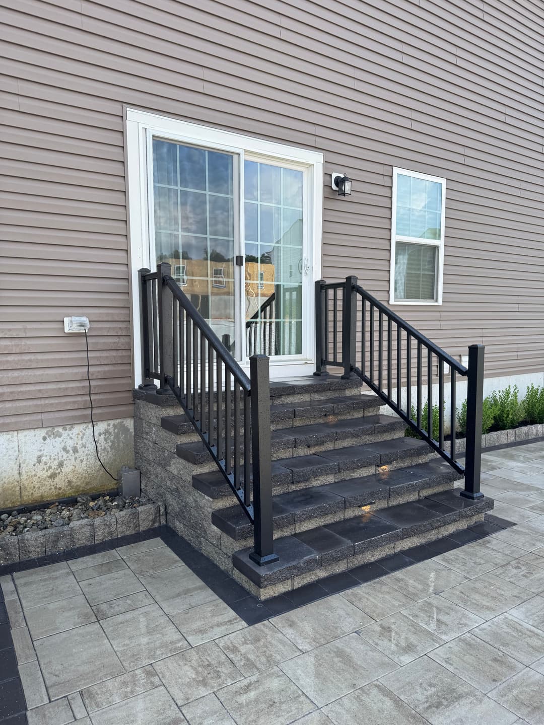 Black metal railing stairs leading to a sliding glass door entry of a modern home.