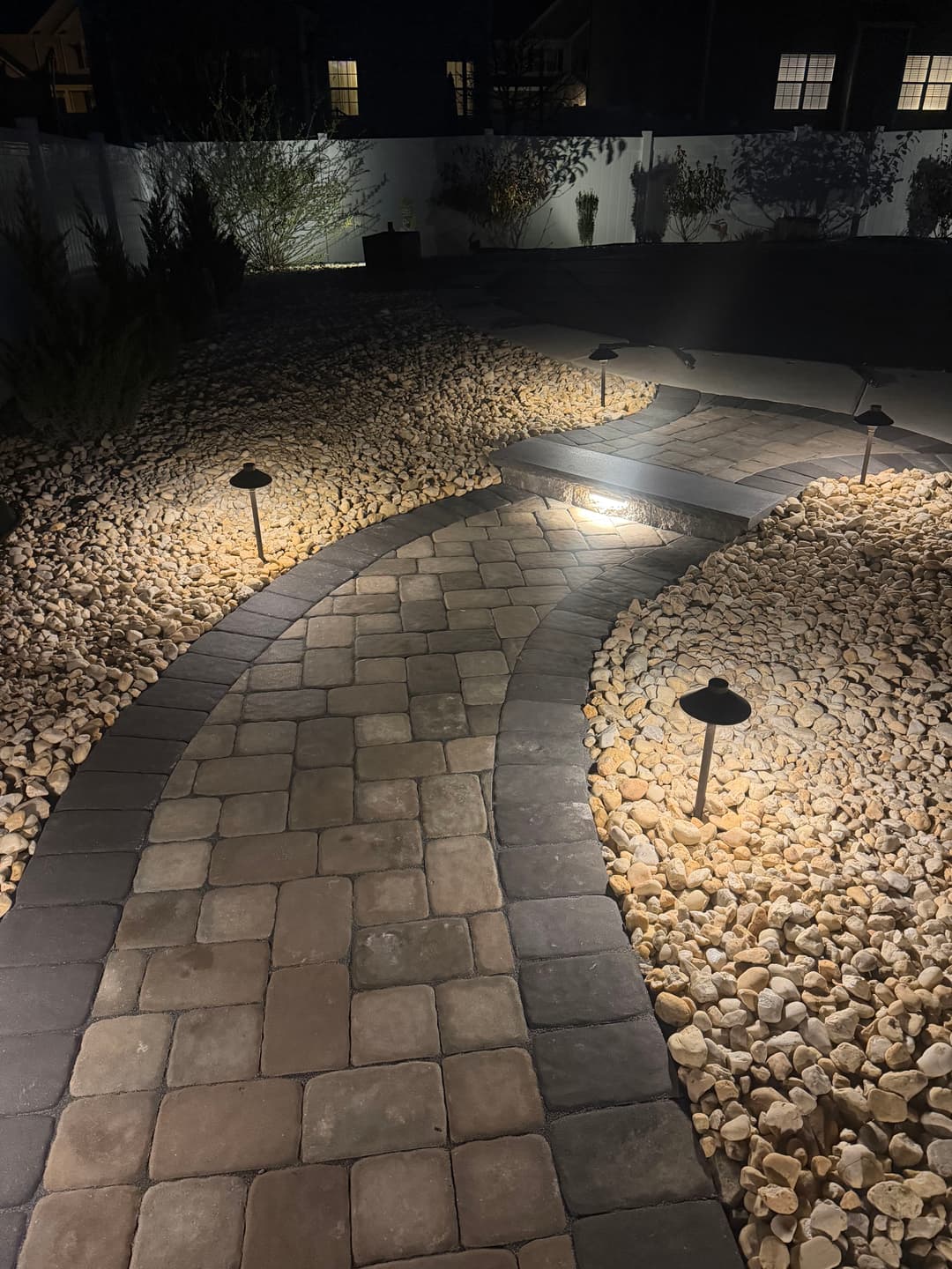 Curved stone pathway illuminated by landscape lighting in a tranquil garden setting.