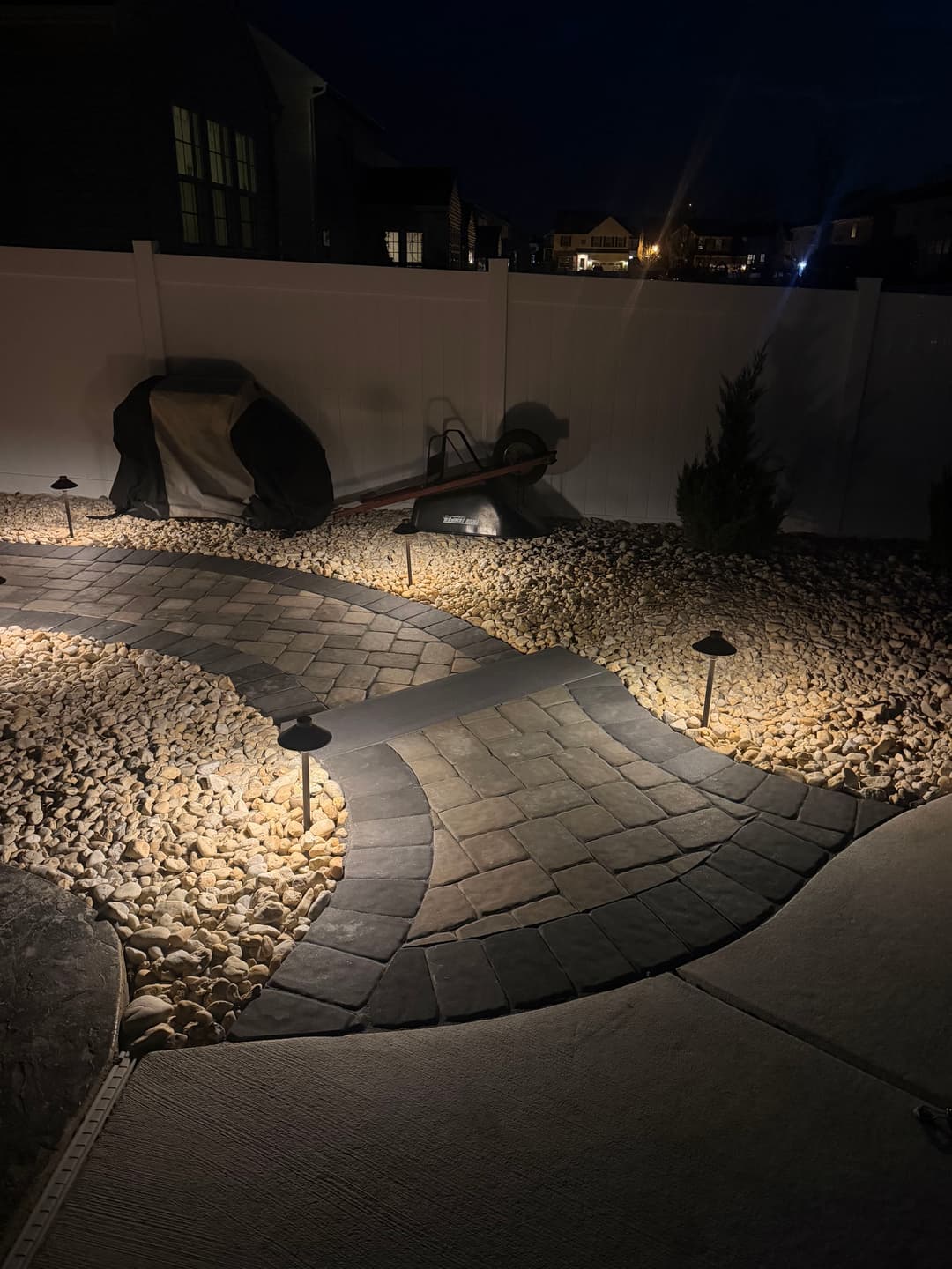 Illuminated stone pathway in a landscaped yard at night with solar lights and decorative rocks.