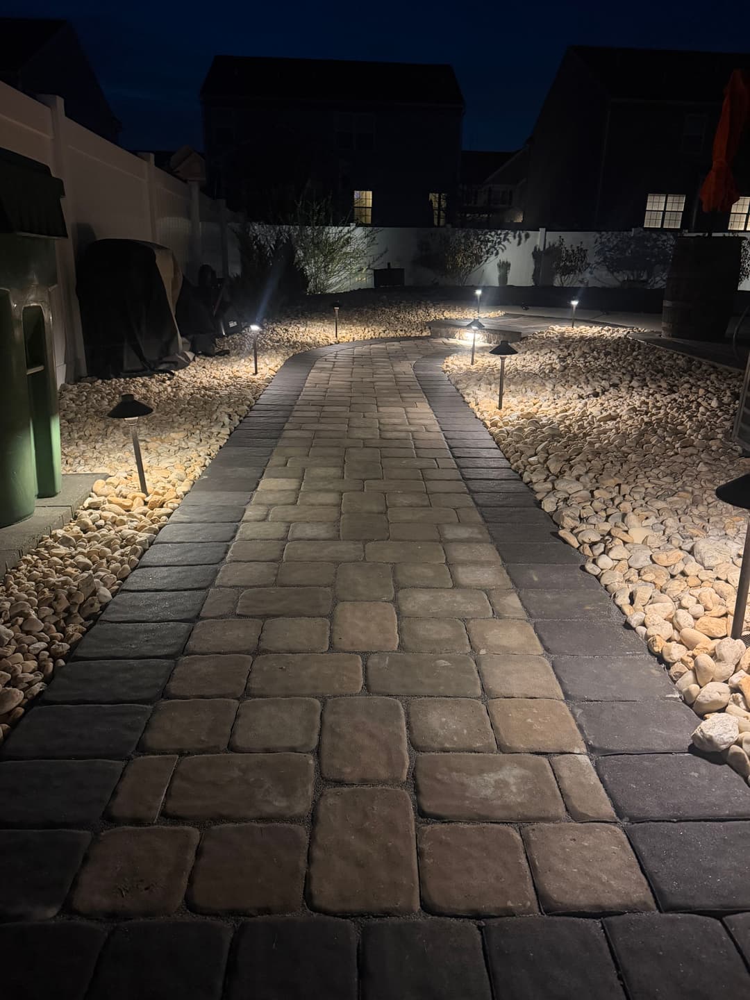 Pathway illuminated at night with stone borders and landscaping lights in a tranquil garden setting.