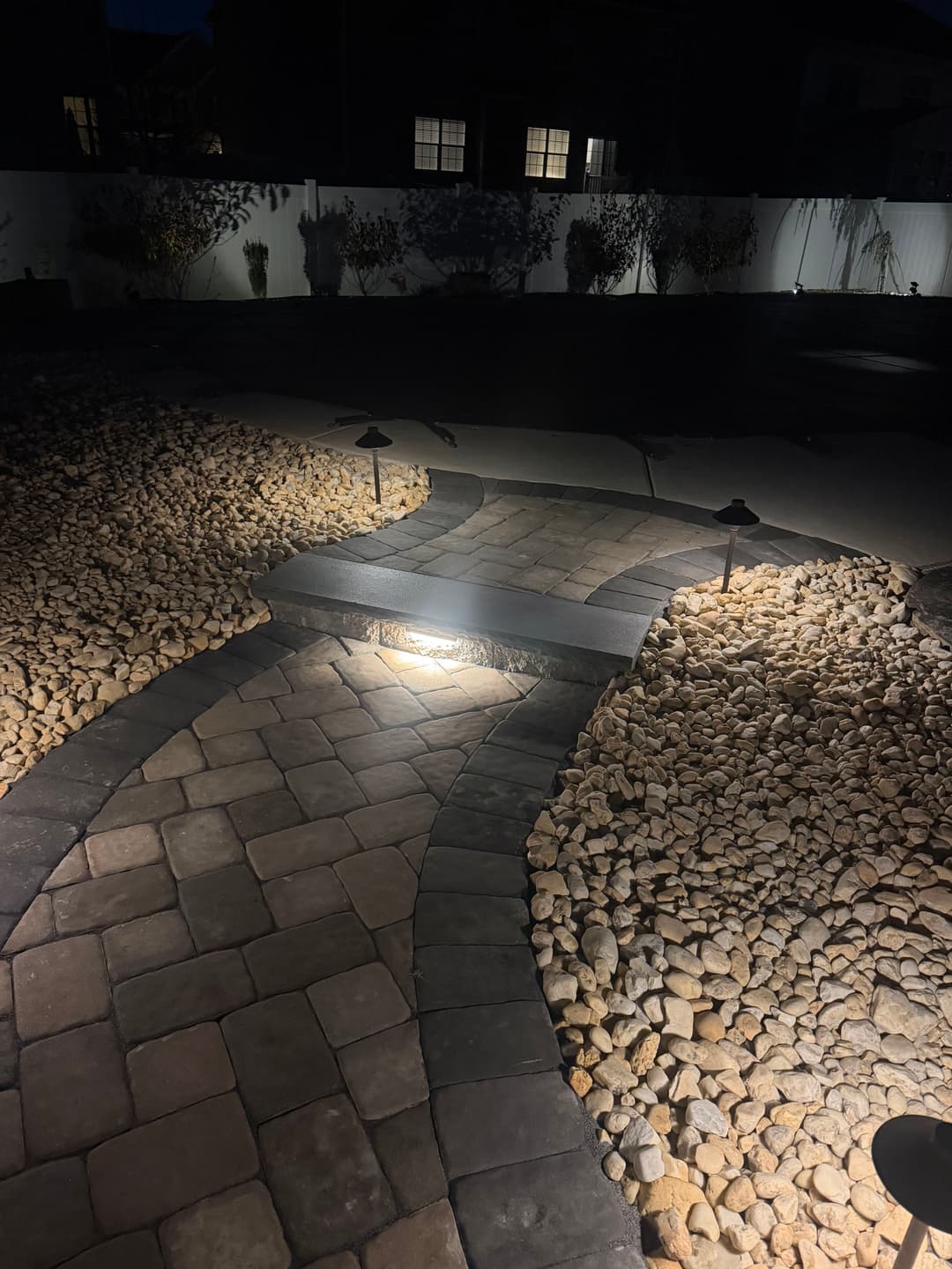 Illuminated stone pathway surrounded by pebbles in a nighttime garden setting.