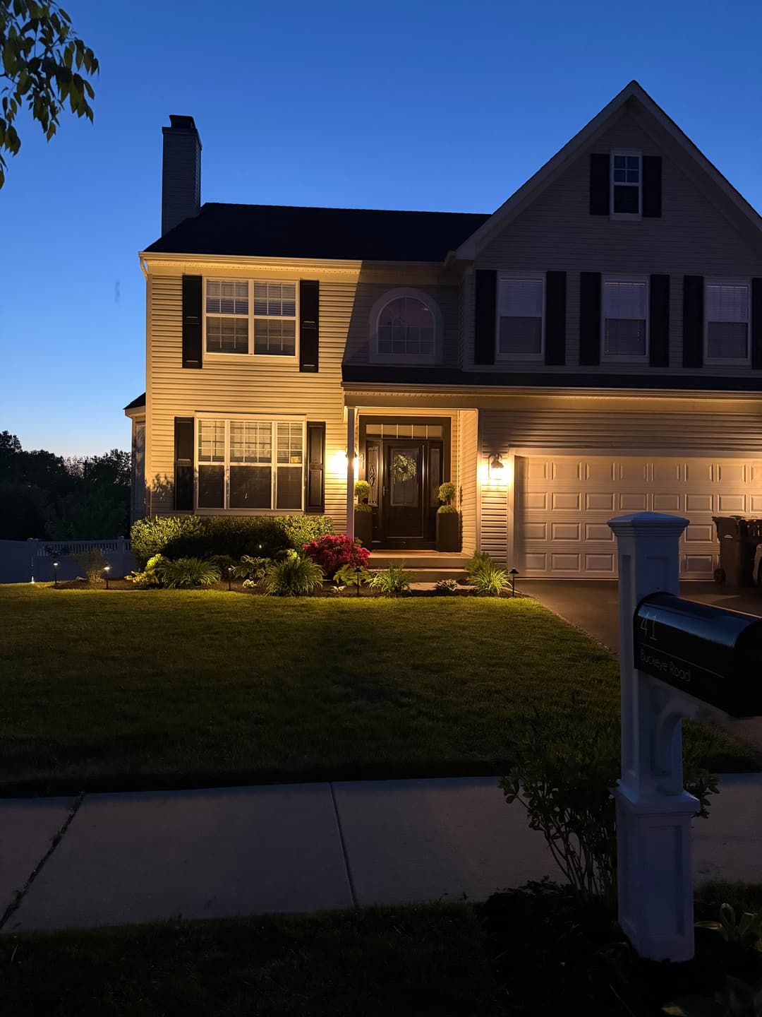 Well-lit suburban home at dusk, featuring a landscaped front yard and inviting entrance.