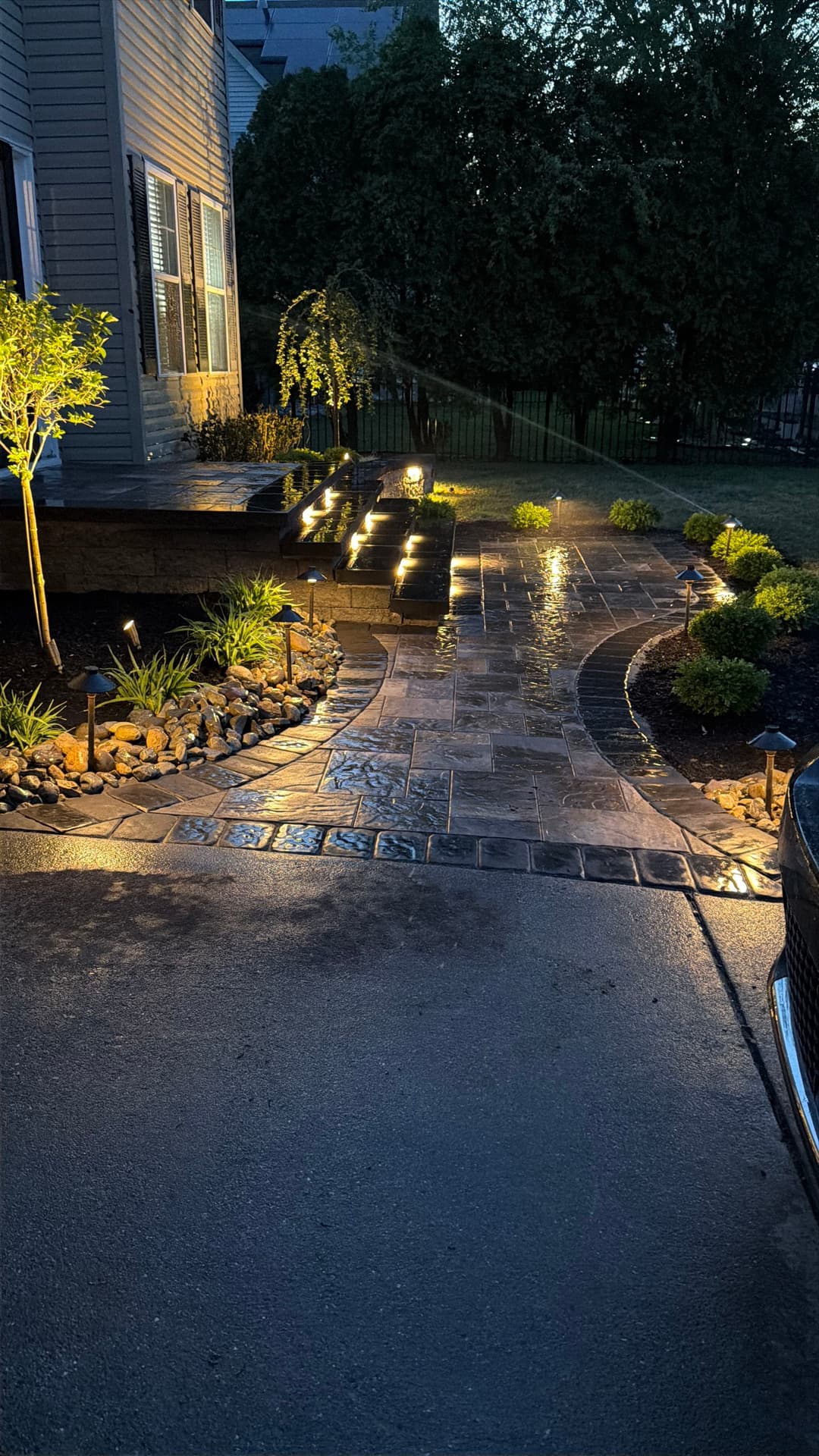 Illuminated front yard pathway with landscaping, stone pavers, and garden lights at dusk.