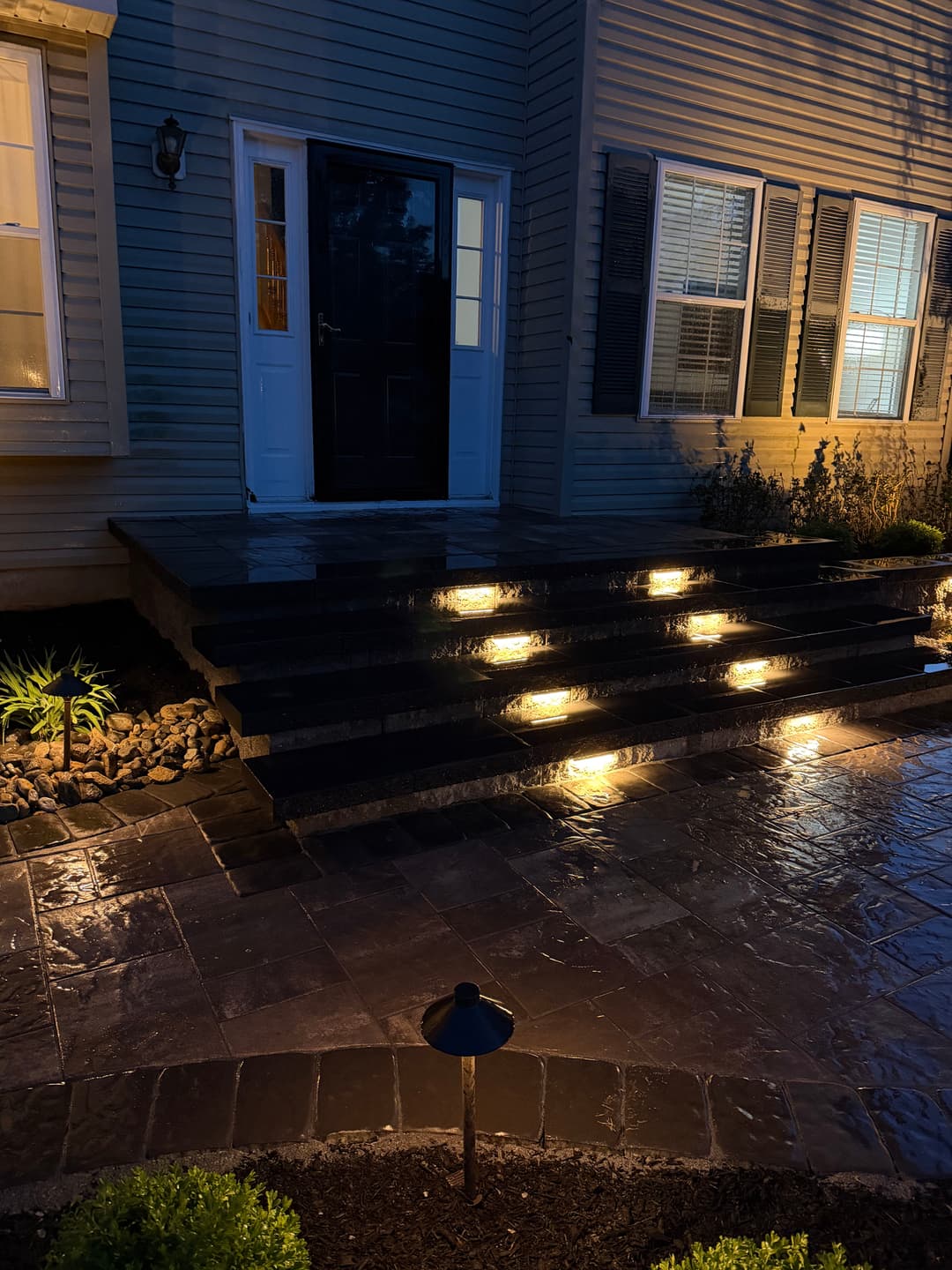 Illuminated stone steps leading to a front door with landscaped garden at night.