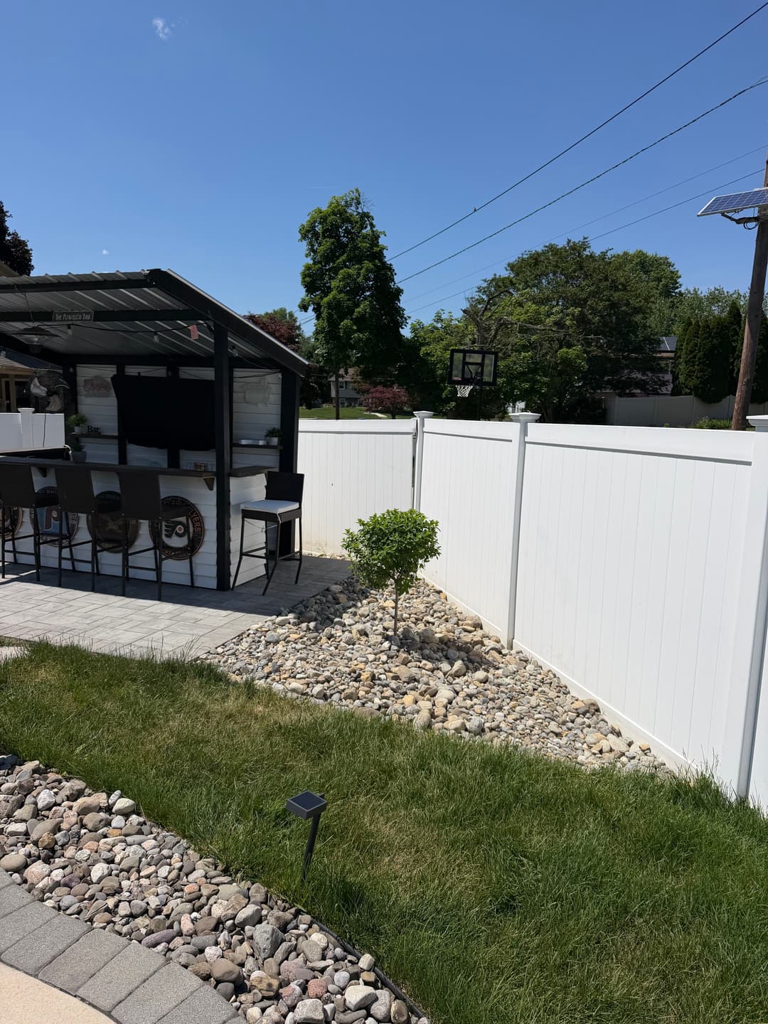 Outdoor patio area with a fenced yard, seating, and landscaping featuring rocks and a small tree.