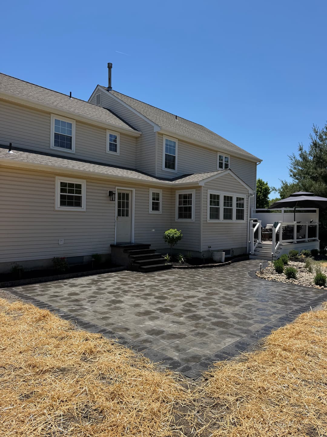 Newly remodeled home exterior with stone patio, landscaping, and clear blue sky.