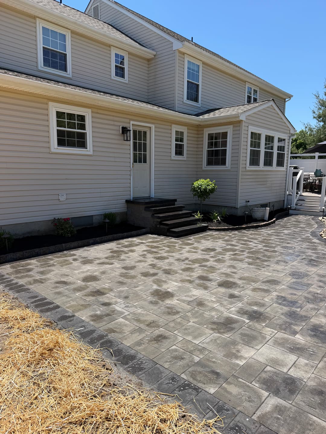 Modern home exterior with paver patio, steps, and landscaping under clear blue sky.