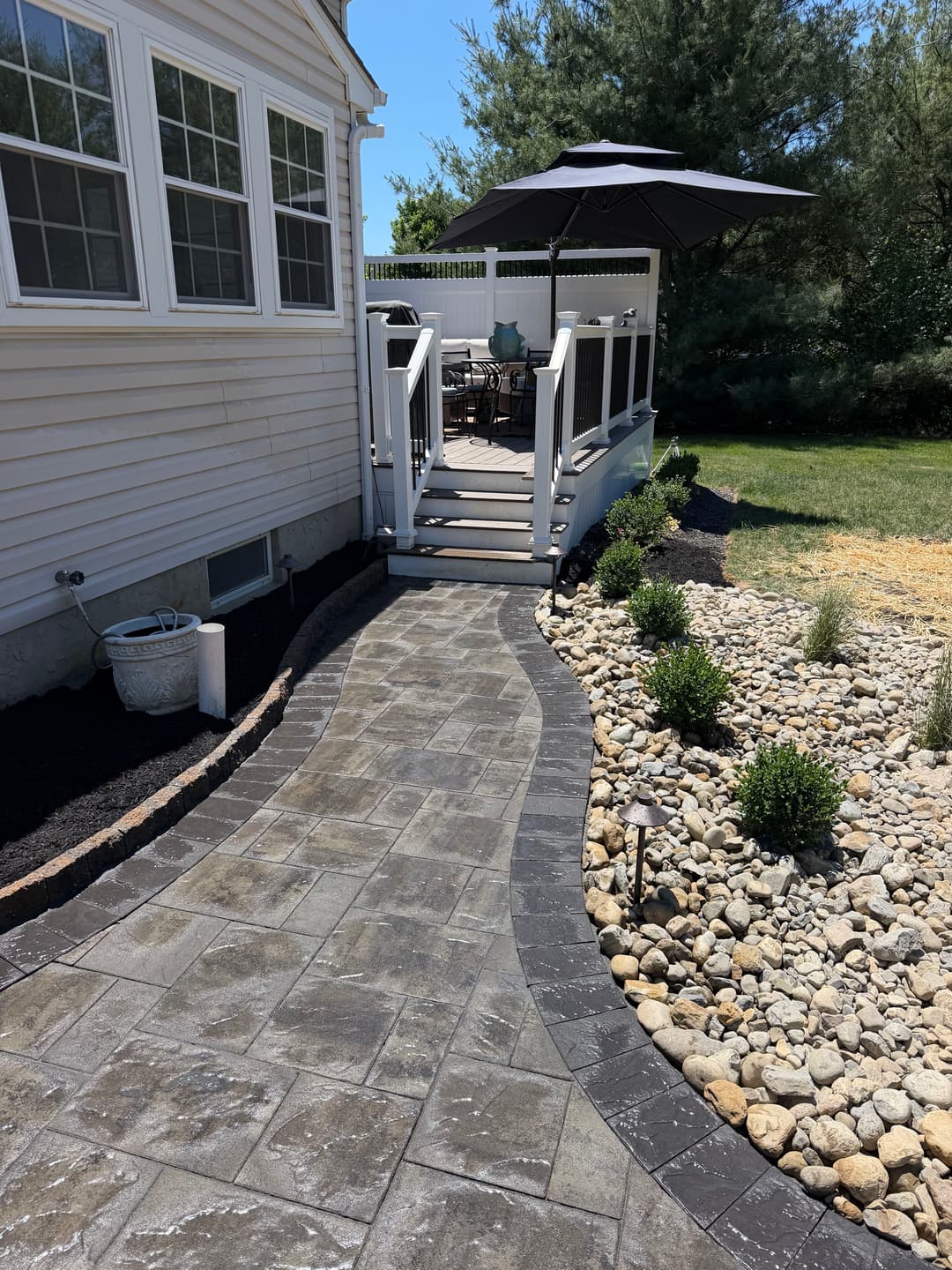 Curved stone pathway leading to a patio with an umbrella and landscaped garden.