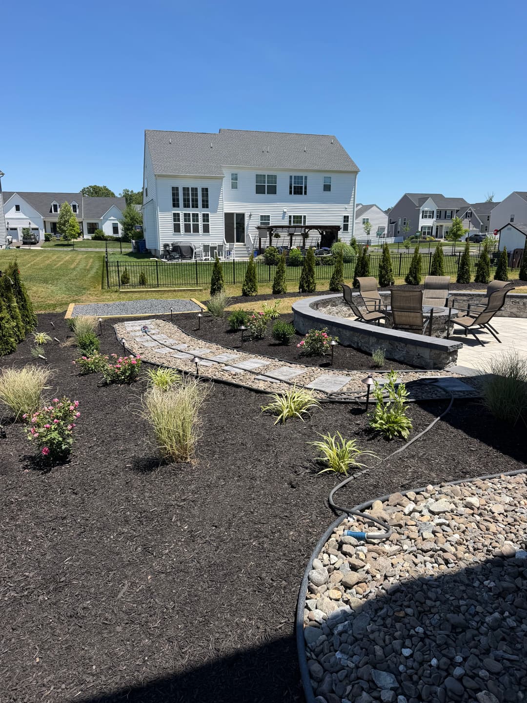 Beautiful backyard landscape with stone path, plants, and seating area near a modern home.