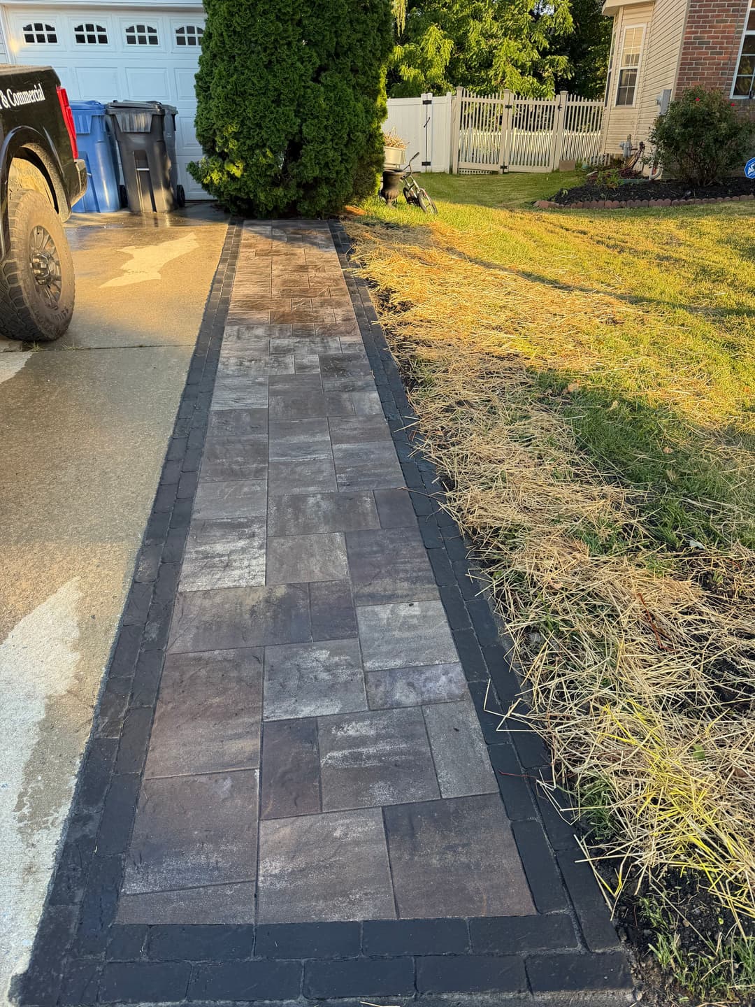 Newly paved walkway with interlocking stone, bordered by landscaping and a parked truck.