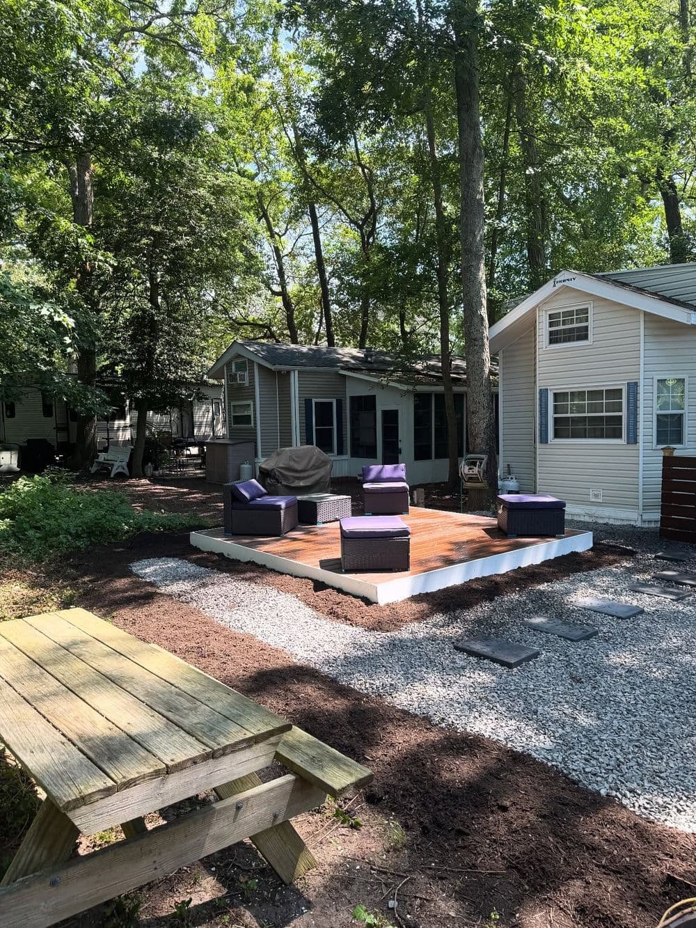 Cozy outdoor patio with purple chairs, picnic table, and gravel landscaping in wooded area.