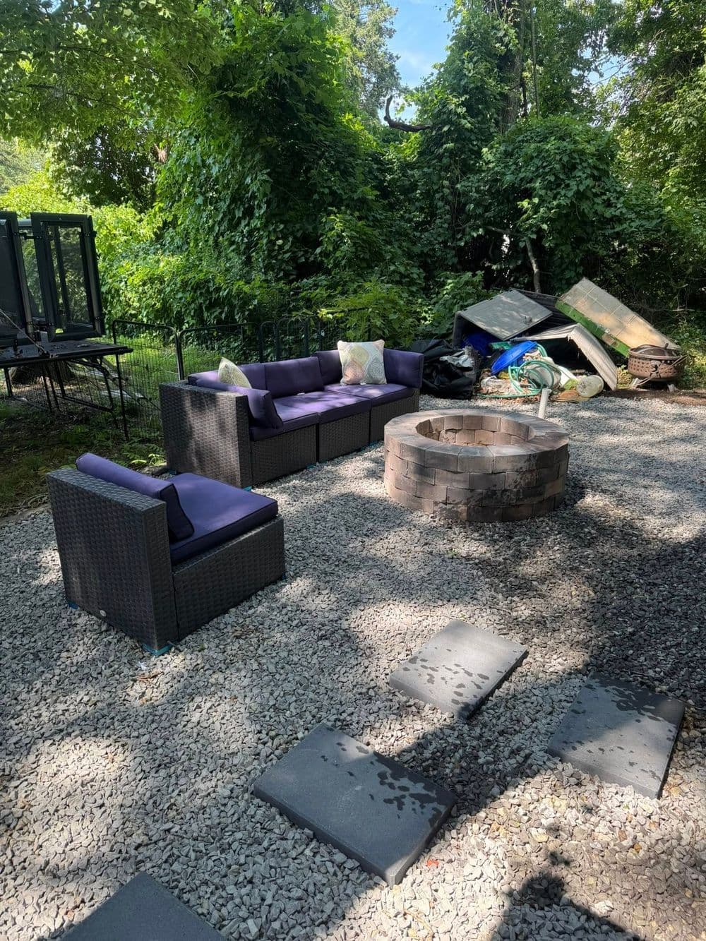 Outdoor fire pit area with modern seating surrounded by lush greenery and scattered stones.