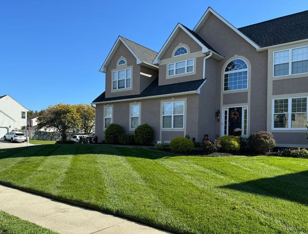 Two-story residential home with landscaped lawn and clear blue sky.