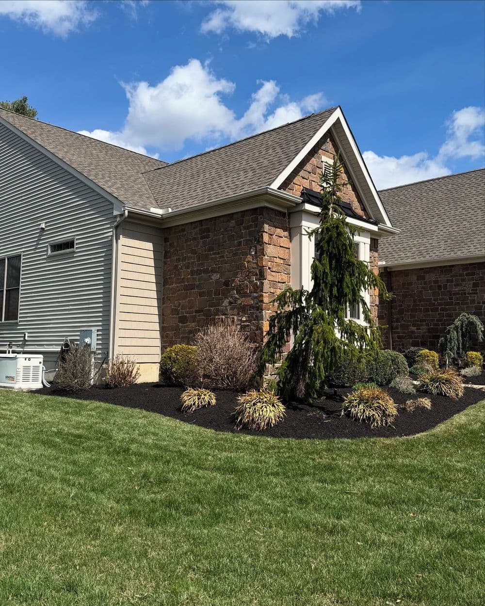 Residential landscaping featuring stone house, manicured bushes, and a vibrant lawn.