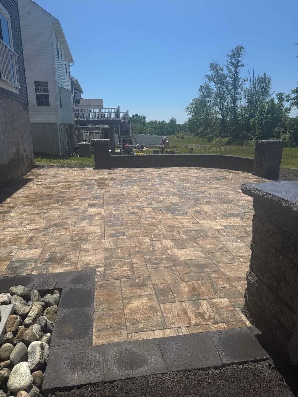 Paved outdoor patio with stone walls, green landscape, and sunny blue sky in the background.