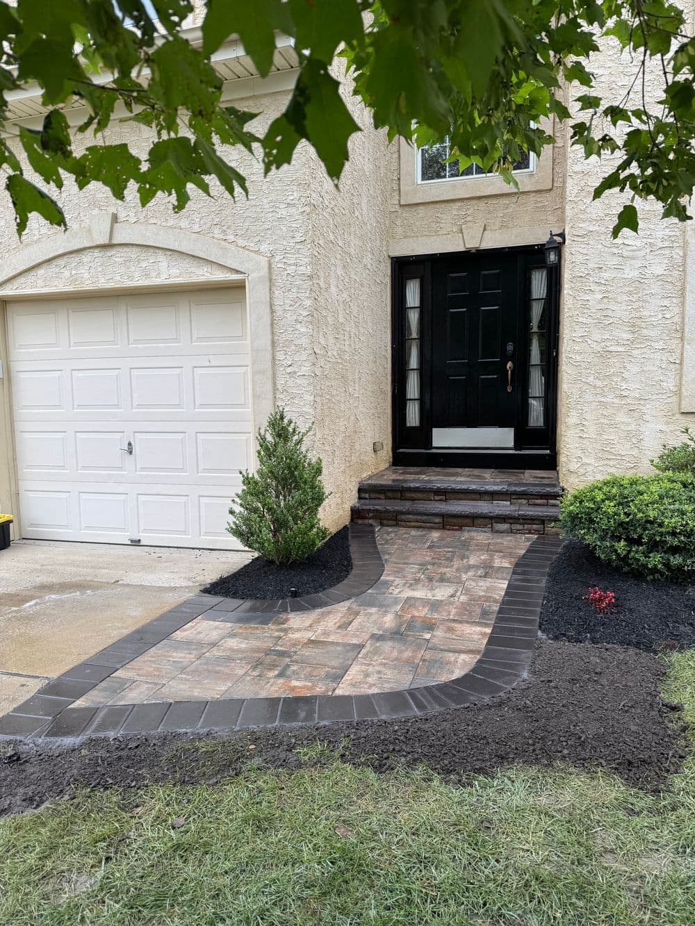 Beautifully paved walkway leading to a black front door, with landscaping and garage.