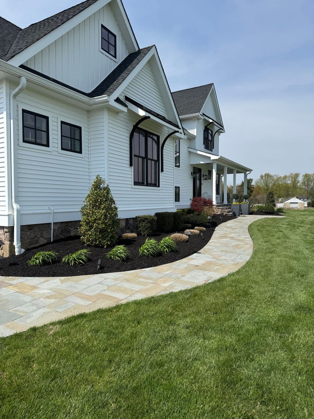 Modern white house with landscaped garden and stone pathway on a sunny day.