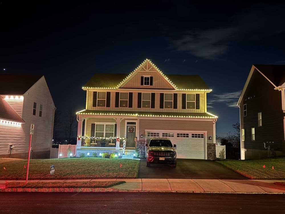 Two-story house decorated with holiday lights at night, parked car in the driveway.