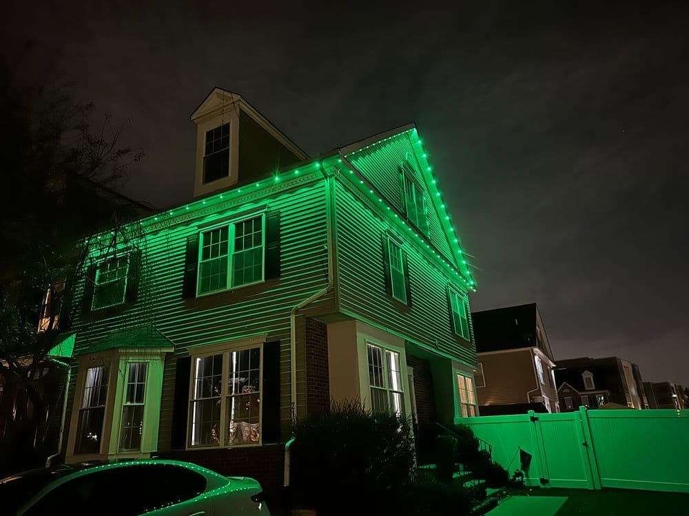 House decorated with green Christmas lights at night against a cloudy sky.