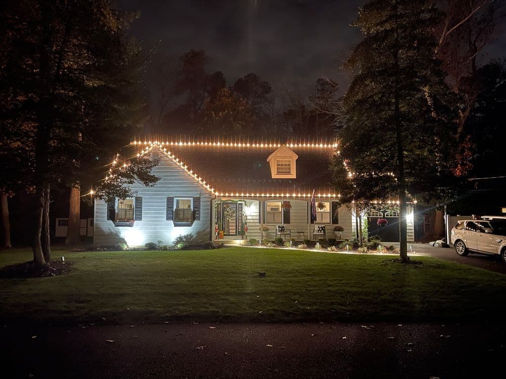 Cozy blue house decorated with string lights at night, surrounded by trees and a grassy yard.