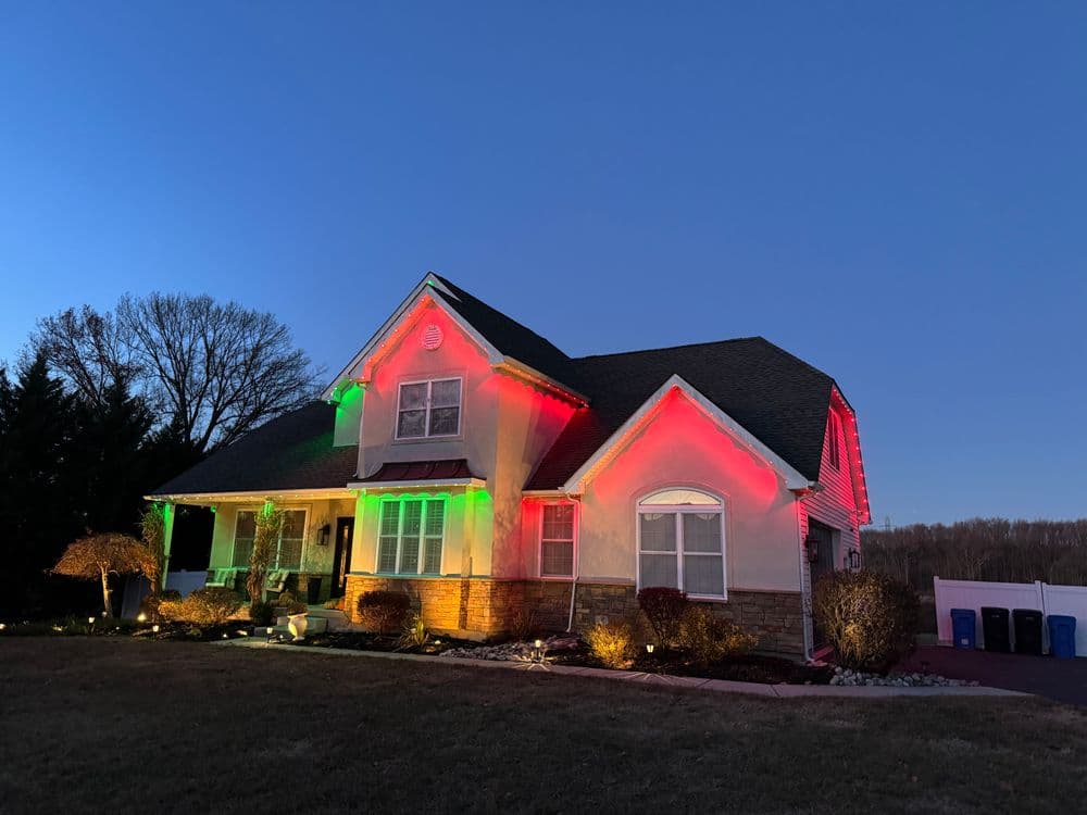 Holiday-lit home at dusk with red and green lights highlighting the architecture.