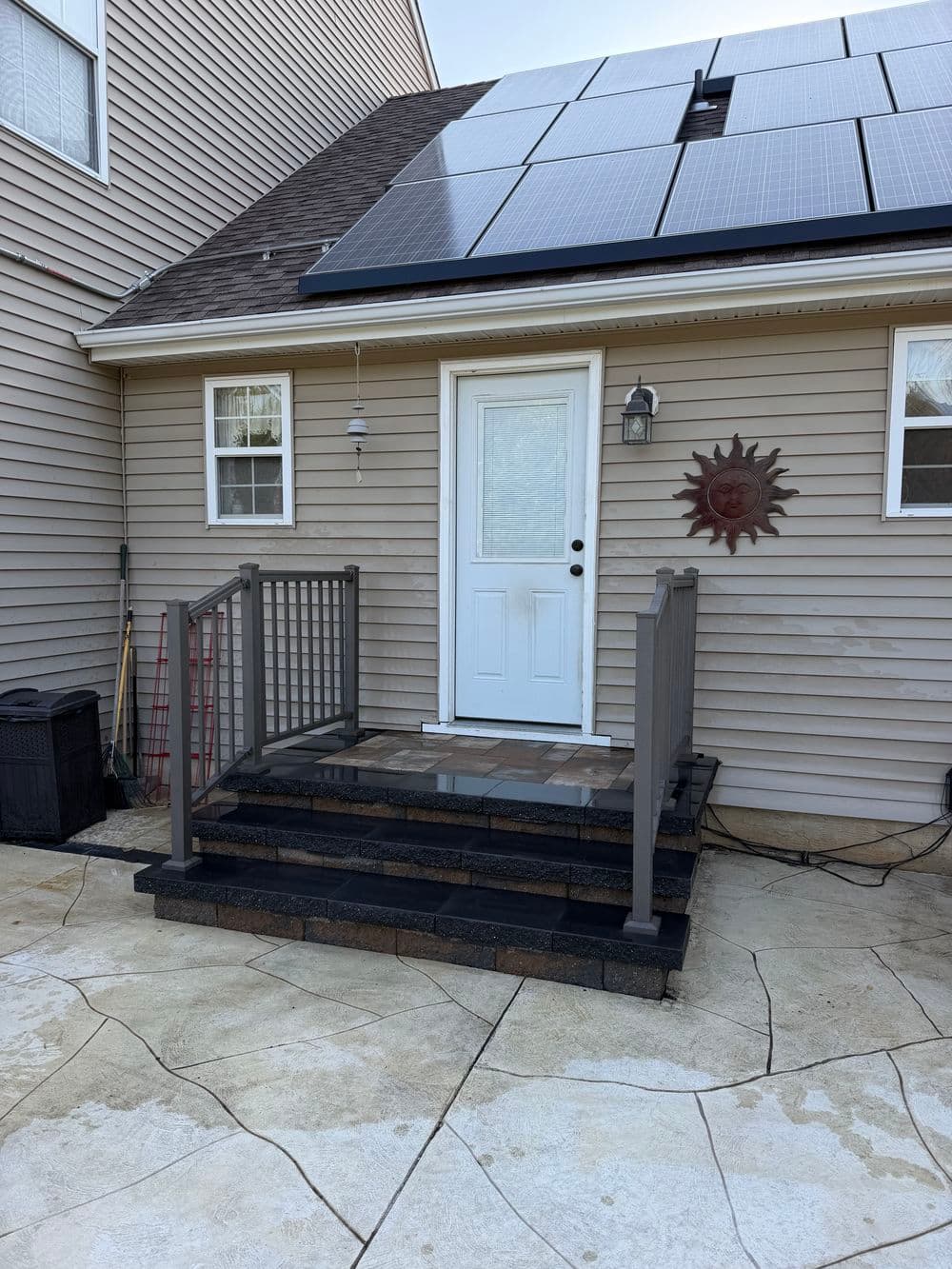 Front entrance with stone steps, railing, solar panels on roof, and decorative sun wall art.