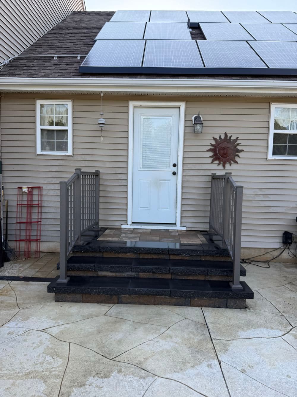 Home entrance with steps, solar panels on the roof, and decorative sun wall art.