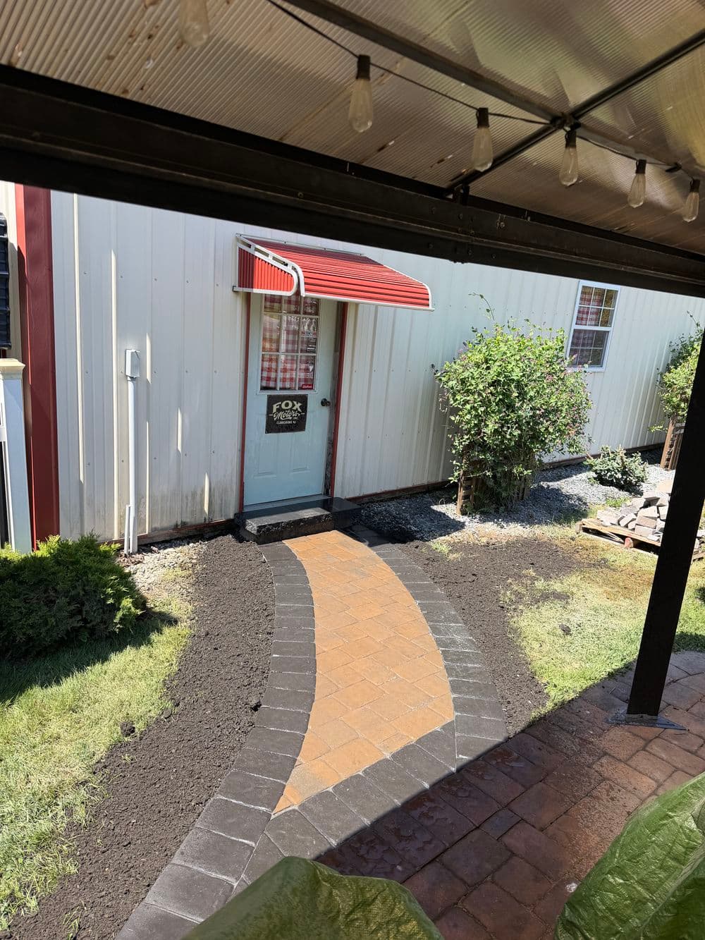 Pathway leading to a door with a red awning, surrounded by freshly landscaped grass and shrubs.