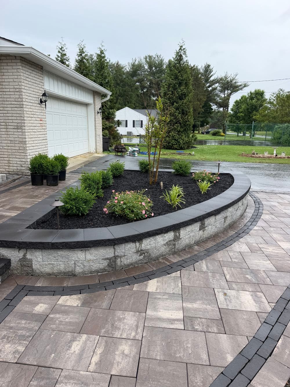 Landscaped patio featuring curved stone planters, flowers, and modern pavers for outdoor appeal.