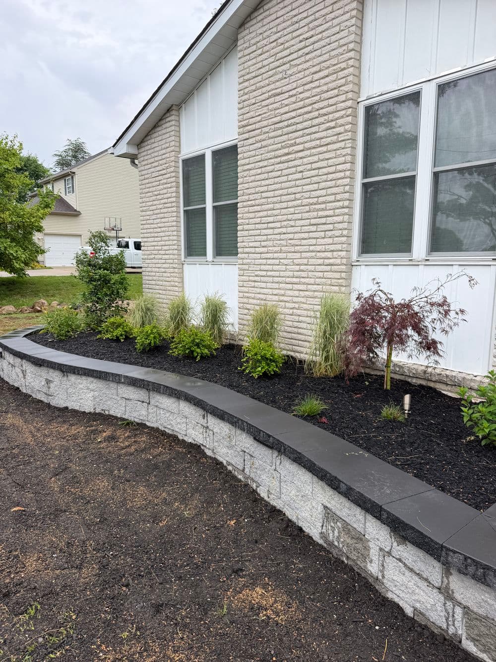 Landscaped garden with black mulch, decorative plants, and a curved stone retaining wall.