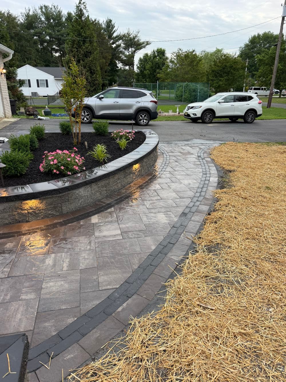 Landscape design featuring curved stone path, flowers, and vehicles in a residential area.