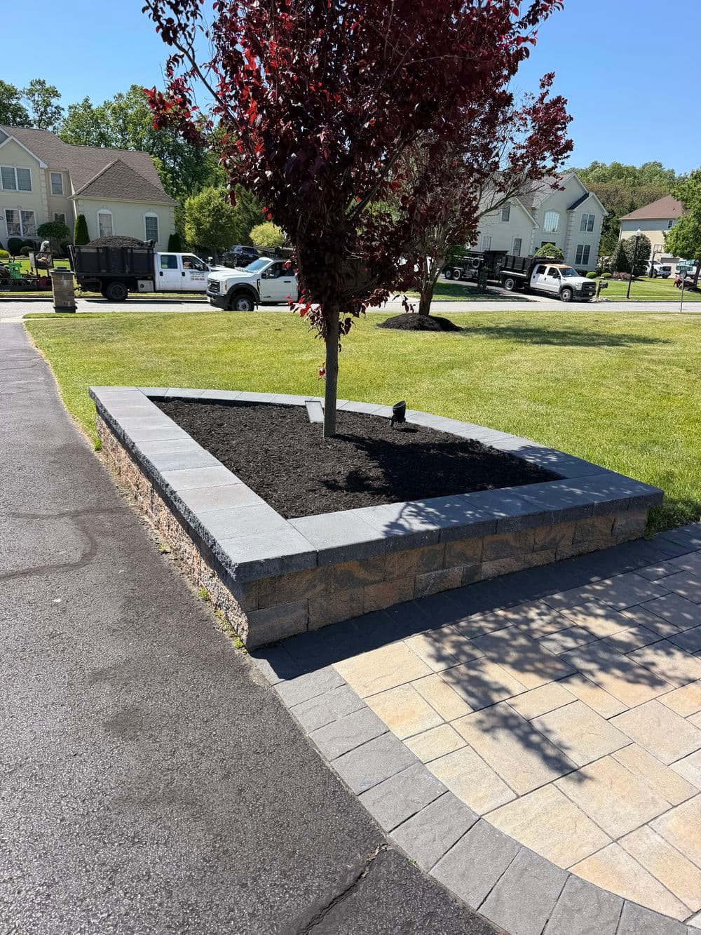 Landscape design featuring a landscaped bed with a tree, stone border, and fresh mulch.