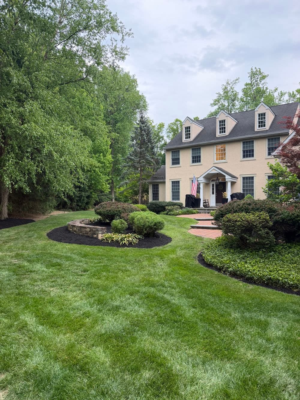 Beautiful landscaped home with American flag, surrounded by lush greenery and well-maintained lawn.